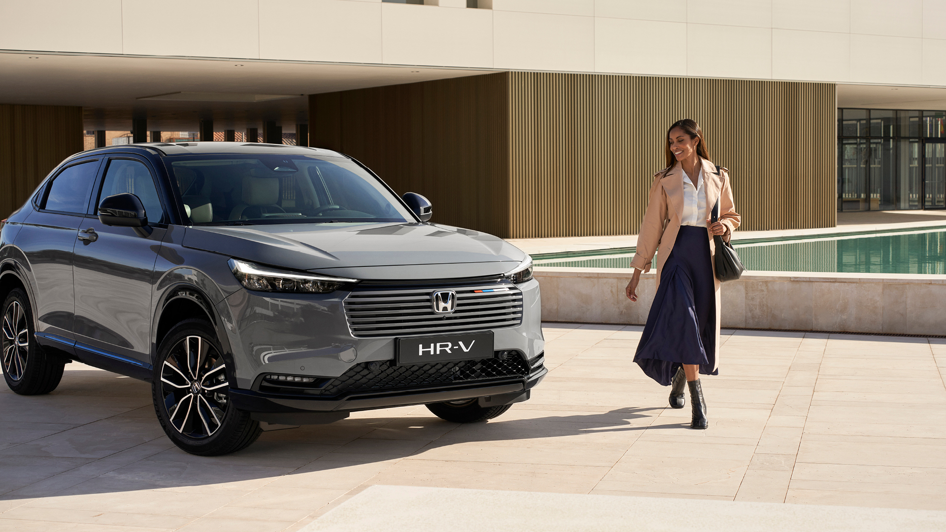 Mujer caminando al lado de un HR-V estacionado en el exterior, junto a un edificio.